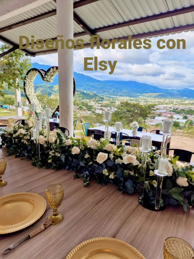 Mesa decorada con flores blancas y velas en una terraza con vista al paisaje.
