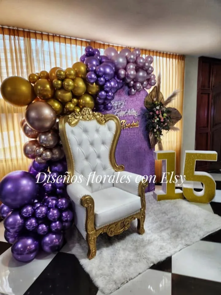 Rincón decorativo de quince años con globos lilas y dorados, sillón blanco y números quince.